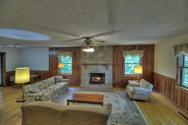 living room featuring light wood-type flooring, a stone fireplace, ceiling fan, and plenty of natural light