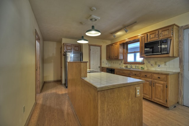 kitchen featuring pendant lighting, tasteful backsplash, a textured ceiling, black appliances, and light wood-type flooring