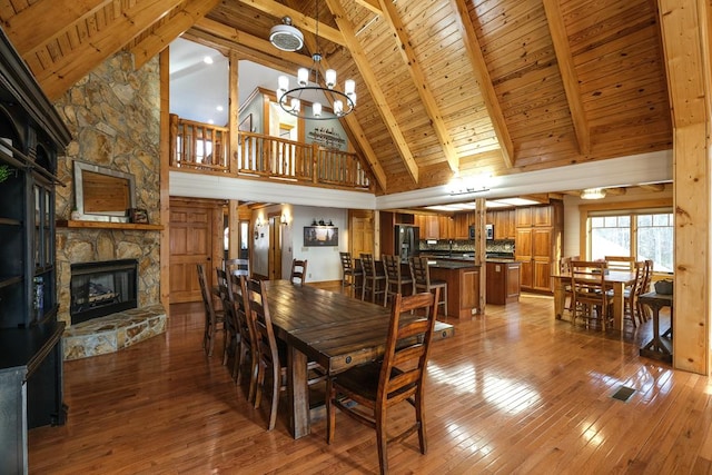 dining room featuring a stone fireplace, lofted ceiling with beams, a chandelier, hardwood / wood-style flooring, and wood ceiling