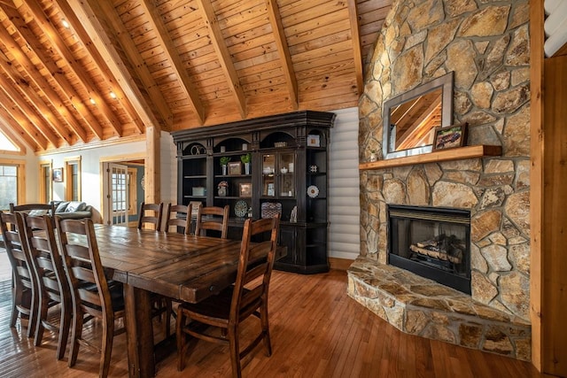 dining area featuring a stone fireplace, wood ceiling, wood-type flooring, high vaulted ceiling, and beam ceiling