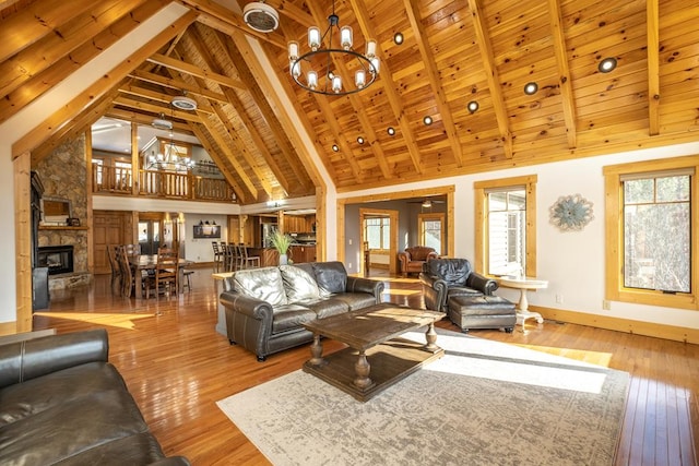 living room with a stone fireplace, an inviting chandelier, high vaulted ceiling, light hardwood / wood-style flooring, and beamed ceiling