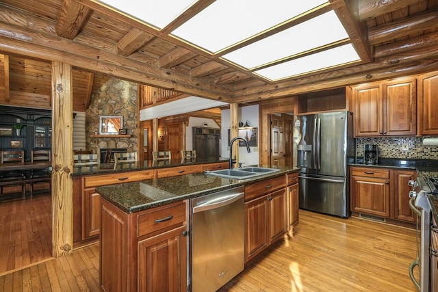 kitchen with sink, dark stone countertops, a kitchen island with sink, stainless steel appliances, and light hardwood / wood-style flooring