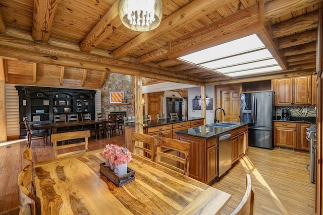 kitchen featuring beamed ceiling, an island with sink, sink, stainless steel appliances, and light hardwood / wood-style flooring