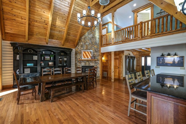 dining area featuring a fireplace, beamed ceiling, wood-type flooring, a notable chandelier, and wood ceiling