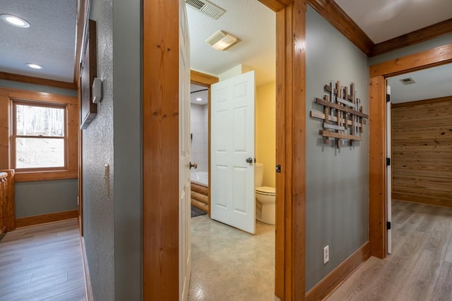 corridor featuring crown molding, light hardwood / wood-style floors, and a textured ceiling