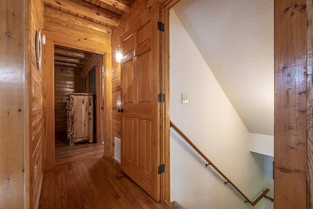 hall featuring beamed ceiling, wood-type flooring, and wooden walls