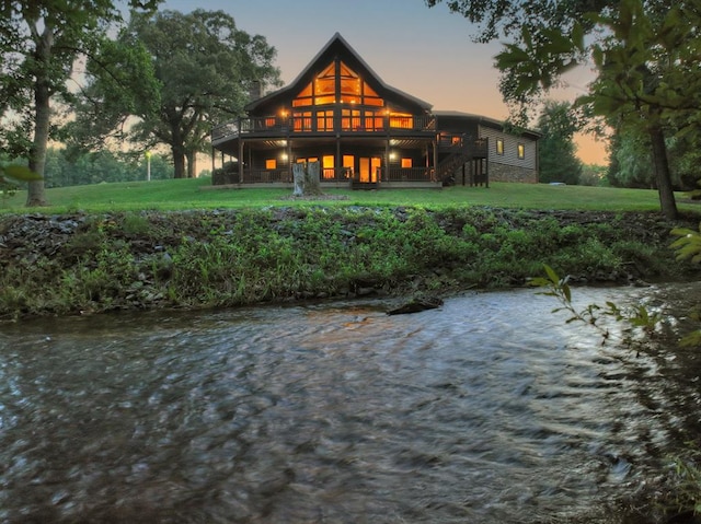 back house at dusk with a deck with water view and a yard