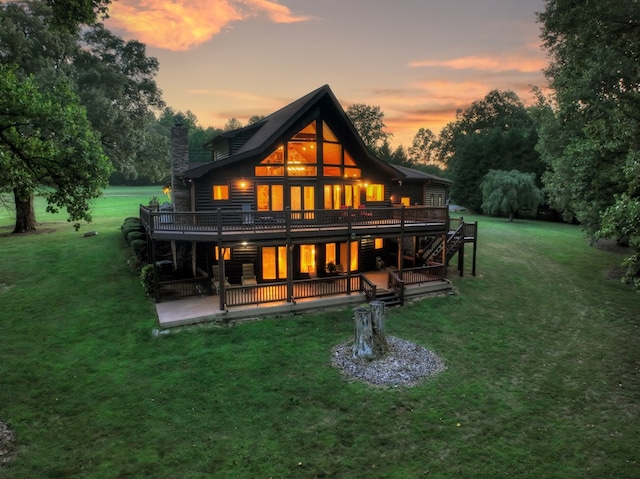 back house at dusk with a deck, a lawn, and a patio