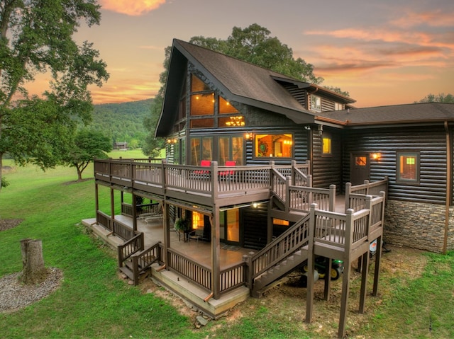 back house at dusk featuring a wooden deck and a lawn