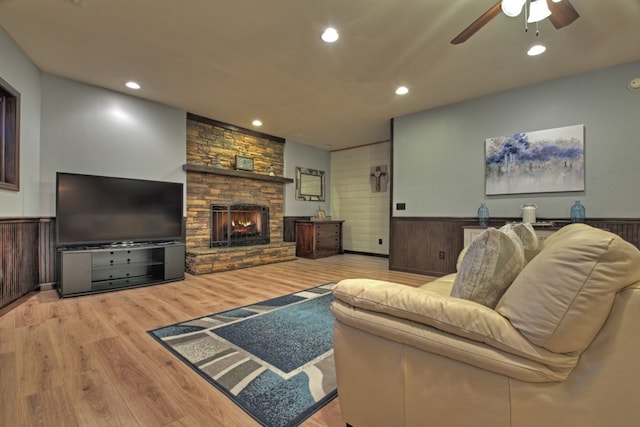 living room with light wood-type flooring, ceiling fan, a fireplace, and wood walls