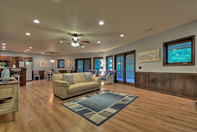 living room featuring ceiling fan, wood walls, and light hardwood / wood-style floors