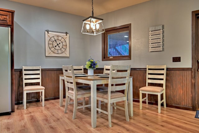 dining room with a chandelier, light hardwood / wood-style flooring, and wooden walls