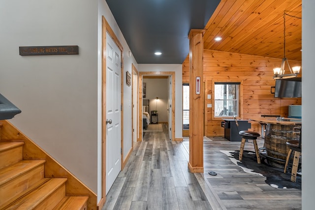 corridor with dark hardwood / wood-style flooring, vaulted ceiling, wooden ceiling, a chandelier, and wood walls