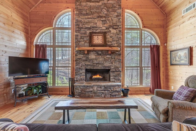 living room featuring a stone fireplace, wood walls, high vaulted ceiling, wooden ceiling, and light hardwood / wood-style flooring