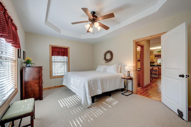 carpeted bedroom with ceiling fan and a tray ceiling