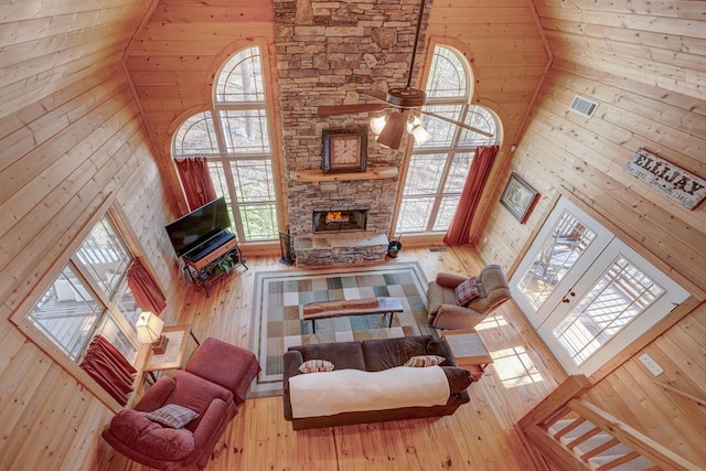 living room featuring high vaulted ceiling, ceiling fan, a fireplace, and wood walls