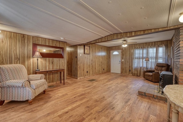 living area with ceiling fan, wood finished floors, wooden walls, and vaulted ceiling
