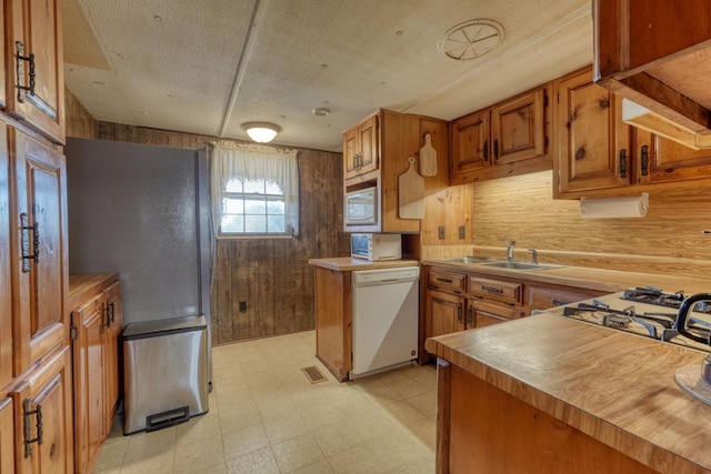 kitchen with wooden walls, white dishwasher, a sink, brown cabinetry, and light floors