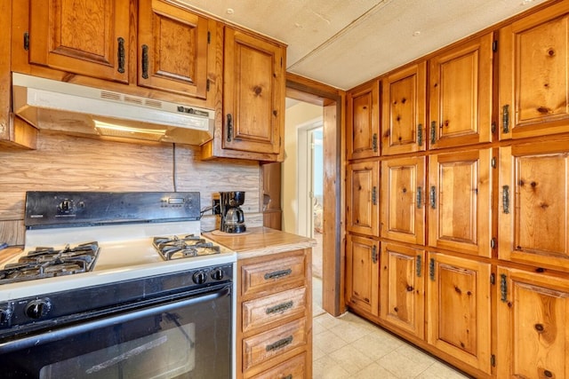 kitchen featuring backsplash, brown cabinetry, under cabinet range hood, and gas range oven
