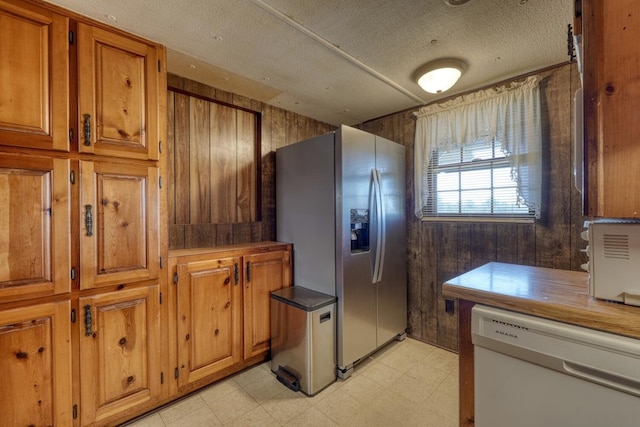 kitchen with brown cabinetry, white dishwasher, light floors, stainless steel refrigerator with ice dispenser, and a textured ceiling
