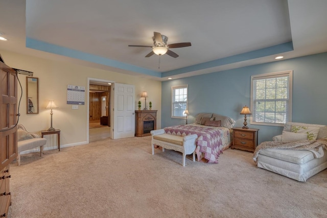 bedroom with a ceiling fan, carpet floors, a glass covered fireplace, a tray ceiling, and recessed lighting