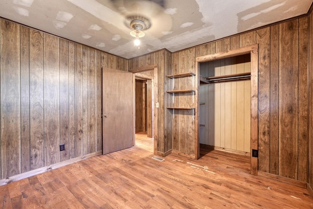 unfurnished bedroom featuring visible vents, a closet, wood finished floors, ceiling fan, and wooden walls