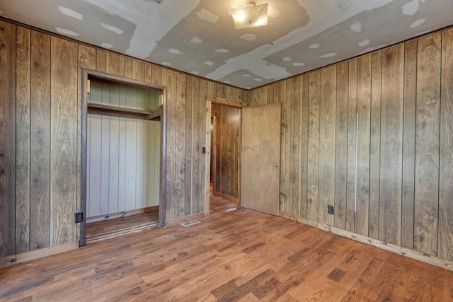 unfurnished bedroom featuring wooden walls, baseboards, and wood finished floors