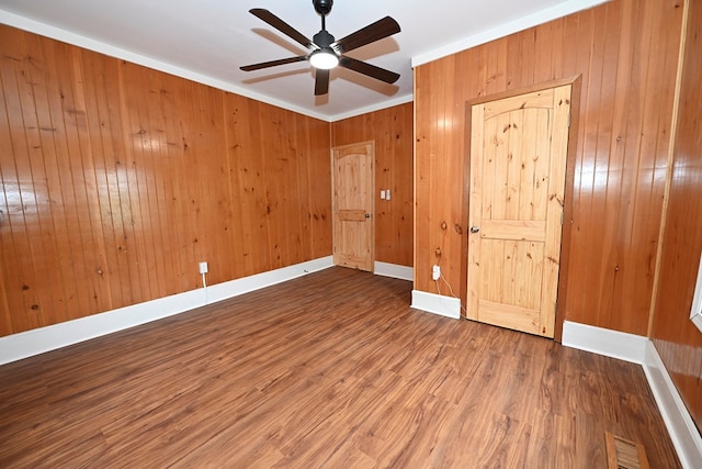 unfurnished bedroom with wood walls, hardwood / wood-style floors, ornamental molding, and ceiling fan