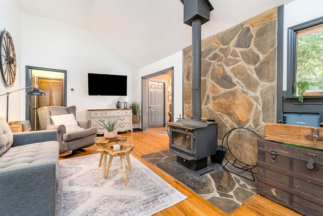 living room featuring wood finished floors, a wood stove, and vaulted ceiling