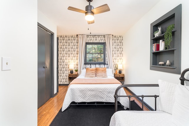 bedroom featuring light wood-style flooring, wallpapered walls, and a ceiling fan