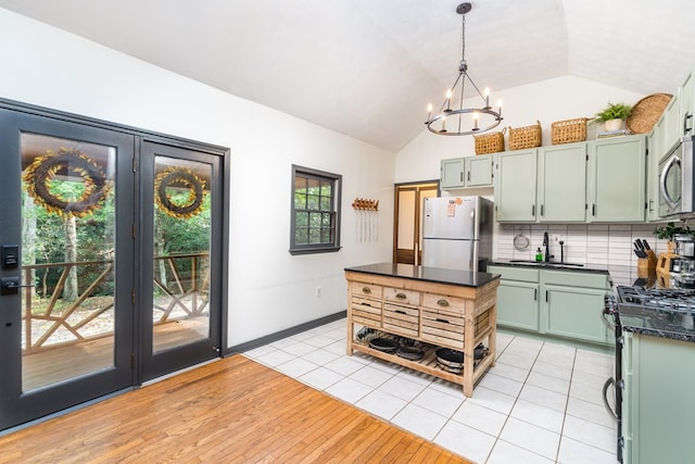 kitchen with stainless steel microwave, dark countertops, freestanding refrigerator, black gas range oven, and a chandelier