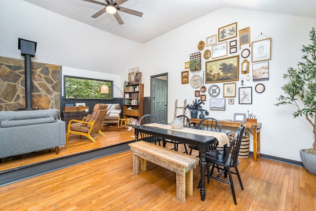 dining room featuring light wood-type flooring, a wood stove, a ceiling fan, and vaulted ceiling