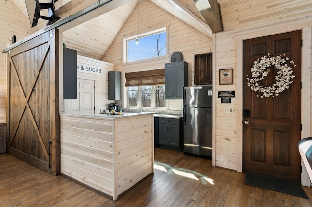 kitchen with dark wood-type flooring, stainless steel fridge, wood walls, and a barn door