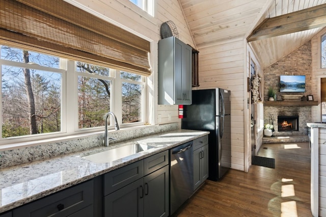 kitchen featuring light stone countertops, dishwasher, a stone fireplace, wooden walls, and gray cabinetry