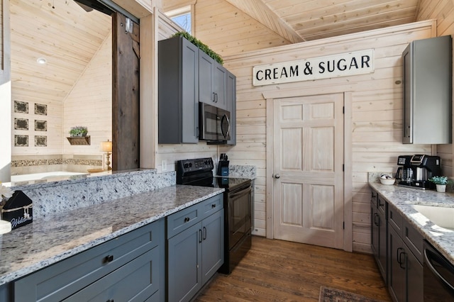 kitchen with light stone counters, dark hardwood / wood-style flooring, black appliances, and wood walls