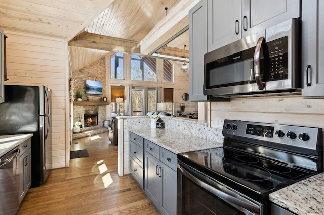 kitchen with a fireplace, wood walls, appliances with stainless steel finishes, wood ceiling, and gray cabinetry