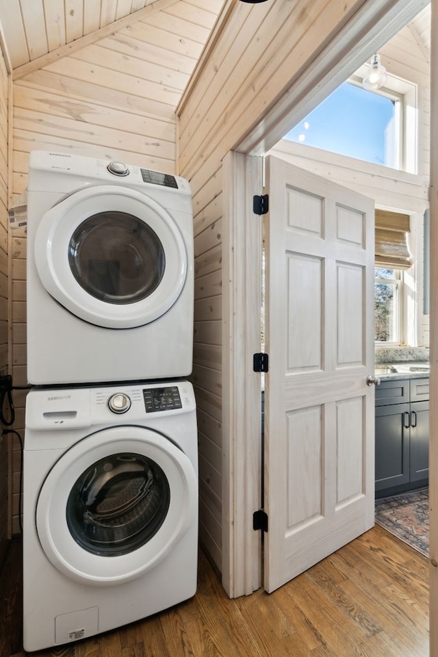 laundry room with light hardwood / wood-style floors, stacked washer / drying machine, wood walls, and wood ceiling