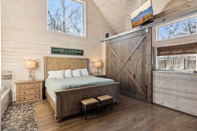 bedroom with high vaulted ceiling, dark hardwood / wood-style floors, a barn door, and wooden walls