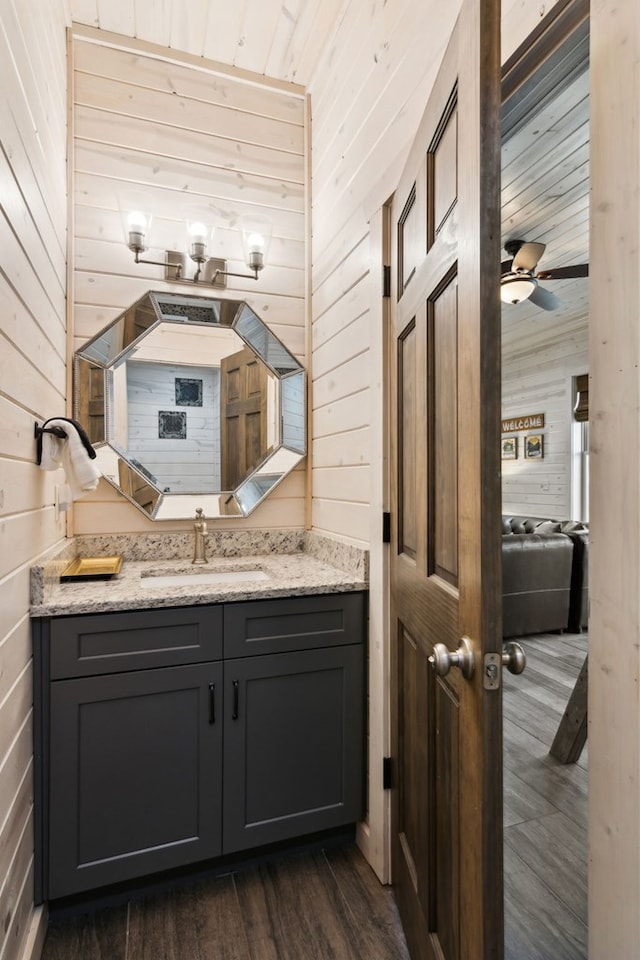 bathroom with ceiling fan, hardwood / wood-style floors, vanity, and wooden walls