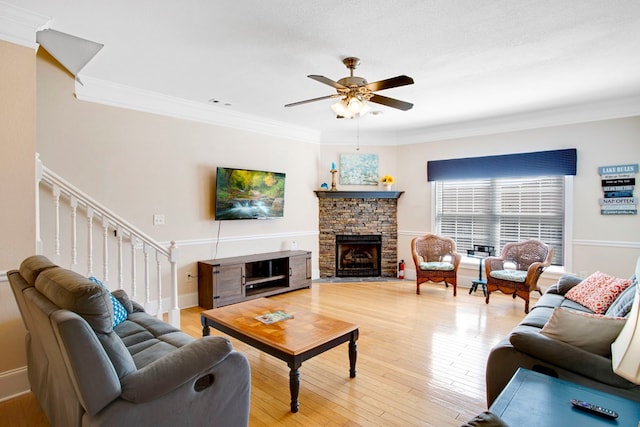 living area with light wood-style flooring, ornamental molding, stairway, a stone fireplace, and ceiling fan