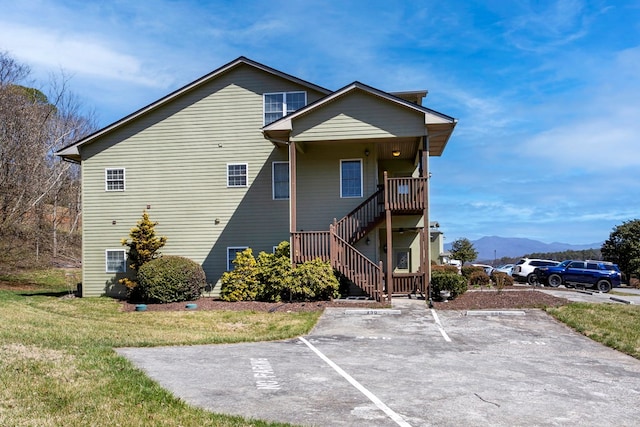 back of house featuring stairway, a lawn, uncovered parking, and a mountain view