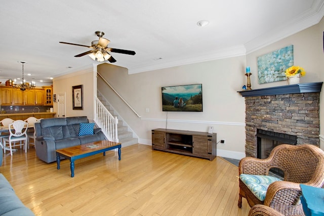 living room featuring light wood-type flooring, ceiling fan with notable chandelier, stairway, crown molding, and baseboards