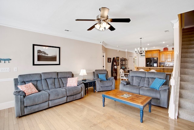 living area with visible vents, ceiling fan with notable chandelier, crown molding, light wood finished floors, and stairs