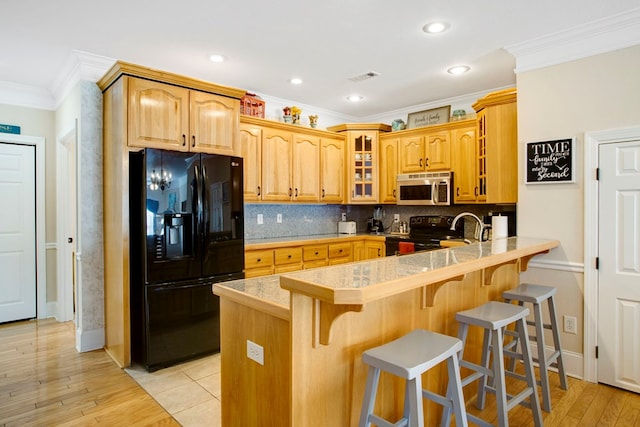 kitchen with visible vents, glass insert cabinets, a breakfast bar area, a peninsula, and black appliances