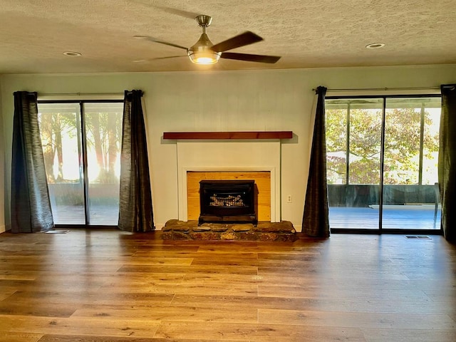 unfurnished living room with light wood-type flooring, a healthy amount of sunlight, a textured ceiling, and ceiling fan