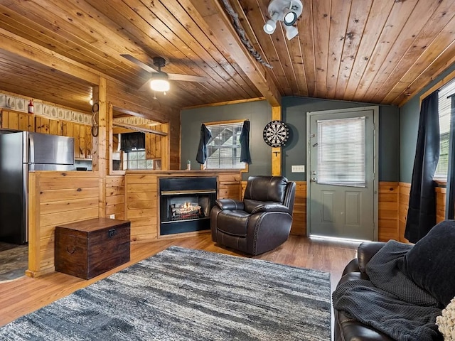living room featuring a wainscoted wall, vaulted ceiling, wooden ceiling, and a healthy amount of sunlight