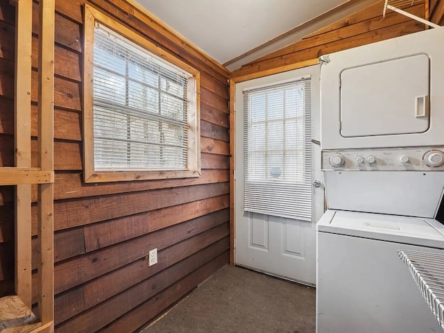 washroom featuring stacked washer / drying machine, carpet flooring, wood walls, and laundry area