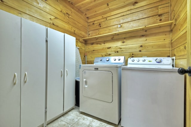 clothes washing area with washer and clothes dryer, cabinet space, and wood walls