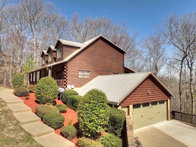 view of property exterior featuring an attached garage, log exterior, and driveway