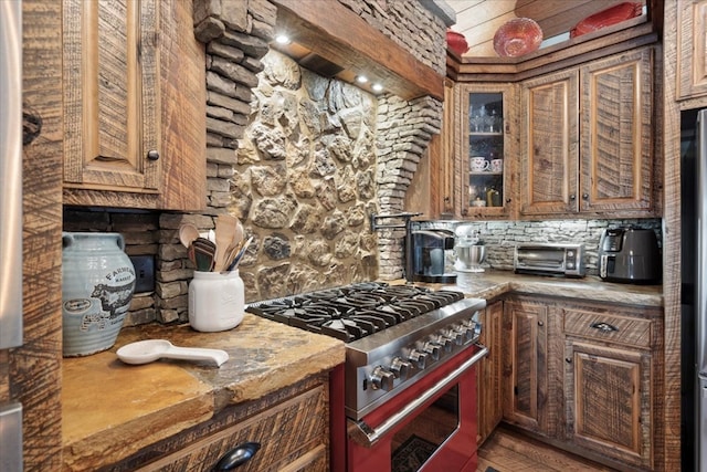 kitchen featuring a toaster, glass insert cabinets, wood finished floors, high end stove, and stone counters